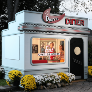 Duffys Diner, a charming retro-style diner playhouse, outside in a backyard. Seen through the window, two children play waiter and customer at the counter.