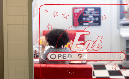 Exterior shot of Duffy's Diner window featuring "Open 24 hours" signage and girl sitting down inside.