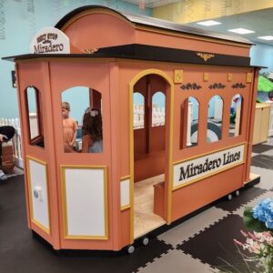 The Main Street Trolley, is clay-colored with custom "Miradero Lines" decals on its side. Inside, a child stands and looks out the window.