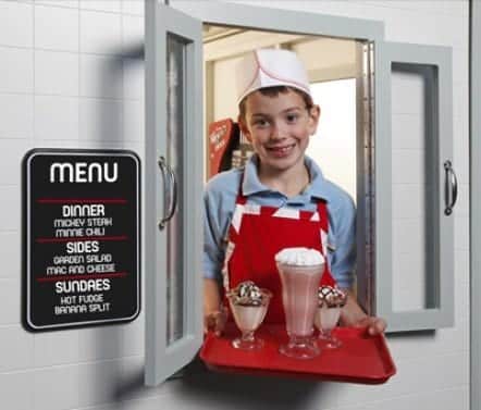 Child serving shakes toy milkshakes outside of drive-through window of the Duffy's Diner playhouse.