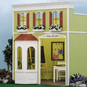 Main Street Gallery playhouse exterior featuring green walls, arched windows with red shutters and blooming window flower boxes. Inside the playhouse, a small white table and a blackboard can be seen.