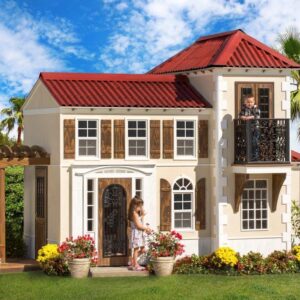 Two children play on the balcony and porch of the Casa de Caramel playhouse, a charming Mediterranean-styled retreat featuring a red tile roof, elegantly designed walls, and wooden shutters.