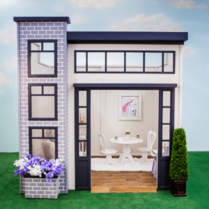 The Uptown Apartment features a wide open front and is shown with a cozy dining area including a round table and chairs. Its exterior is adorned with charming brickwork, large windows, and a flower box with potted plants.