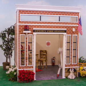 Front view of the Uptown Fire Station playhouse with its hose and reel as well as some decorative furniture and decor.