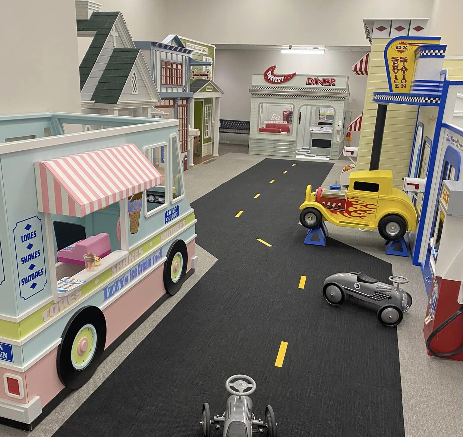 An ice cream truck playhouse sets along a road with a number of playhouses in themes from diner to vet to gas station in this indoor playcenter of a church.