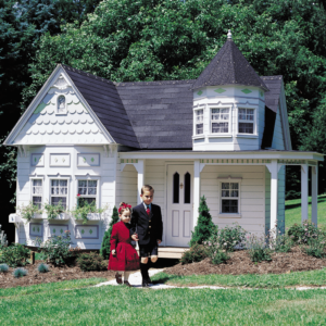 Well-dressed children walk along the path from their grand victorian playhouse which features a turret, stained glass window and many decorative elements.