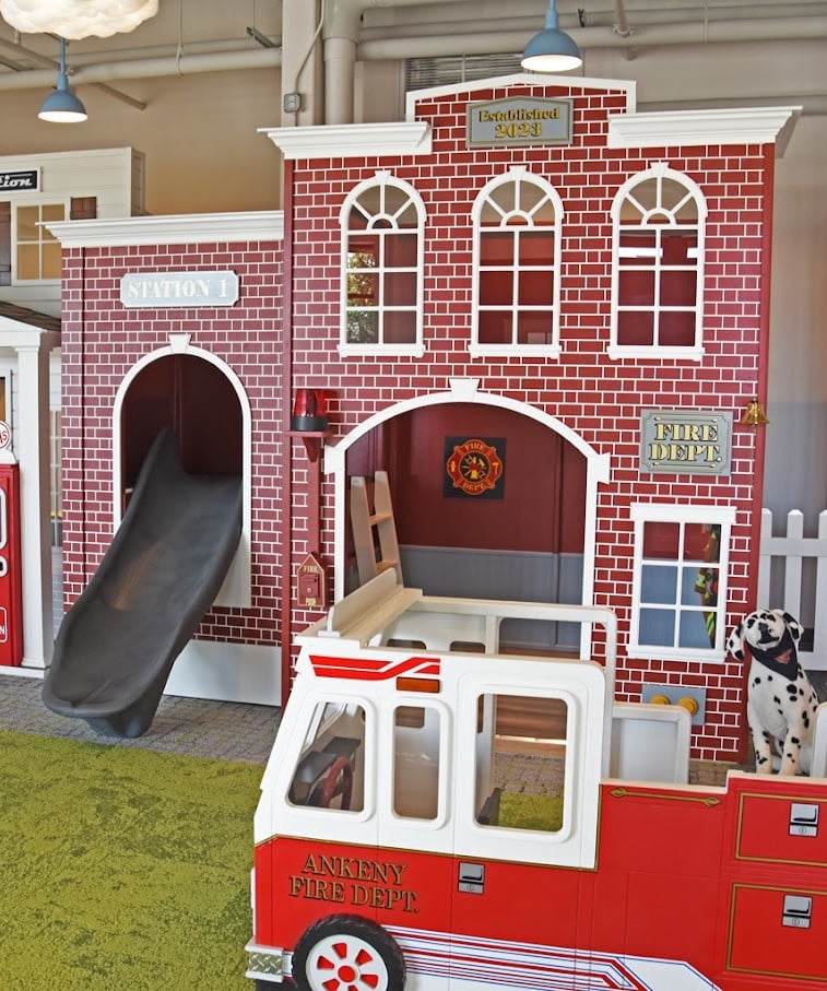 A Fire Station playhouse with a wing housing a slide, and a kids fire truck as part of a large indoor commercial play space.