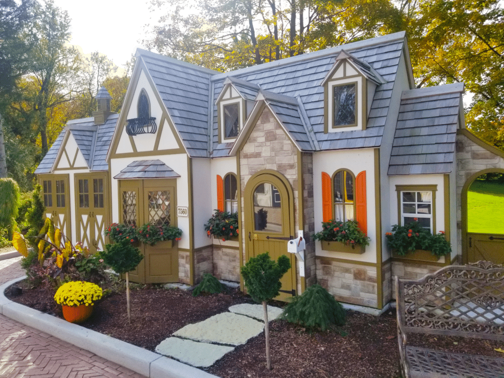 A custom residential playhouse in tutor-style. Features beige walls, stone veneer base, and green and orange trim.