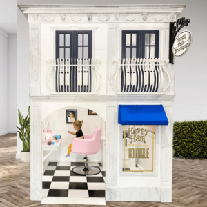 A lovely Beauty Salon playhouse with a small child sitting in a salon chair while she pretends and plays in this playhouse built for use in an indoor play setting.