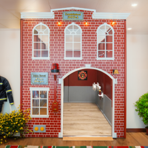 A Main Street Firehouse displaying a facade of faux red brick, an interactive revolving emergency light, a bell and a hose and reel, is the perfect addition to any pretend town or village play space.