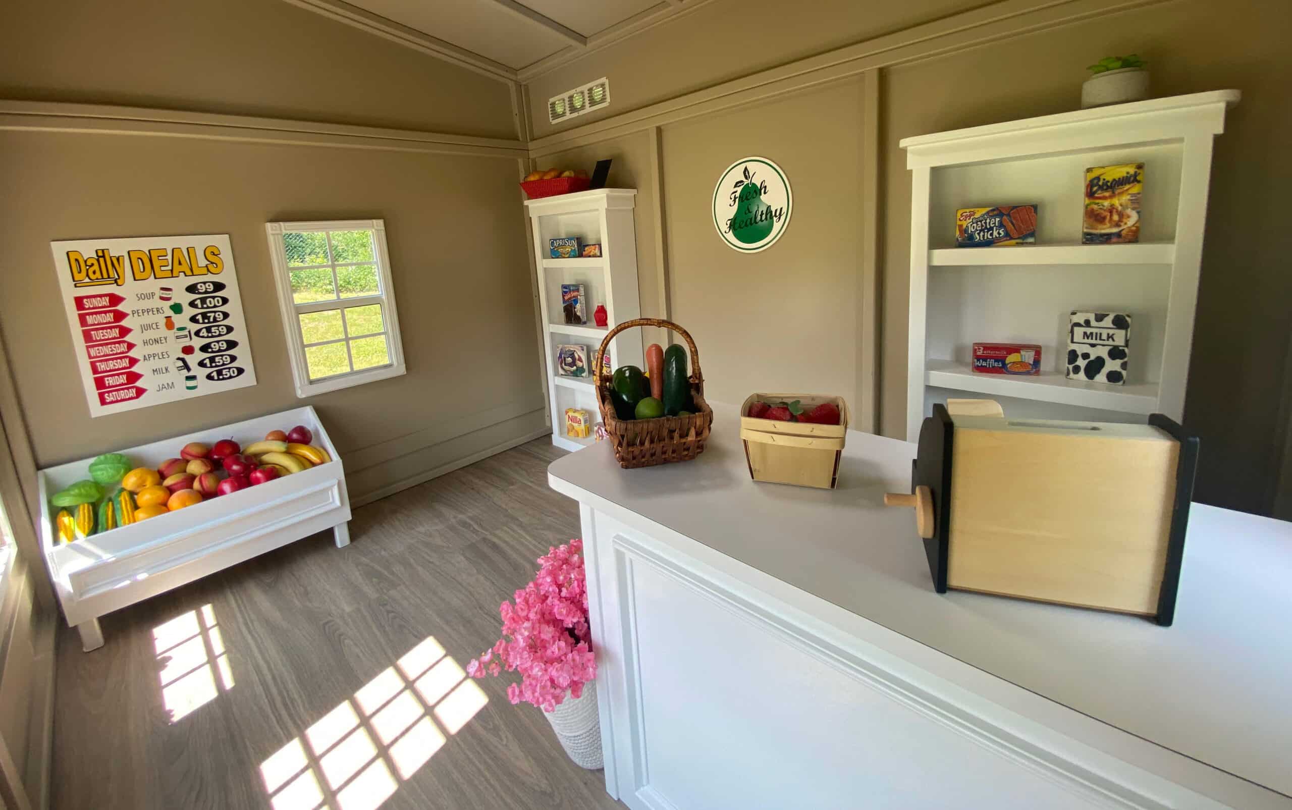 An inside view of an outdoor grocery market playhouse for children showing the custom made wooden furniture consisting of shelves, counters and a vegetable stand.