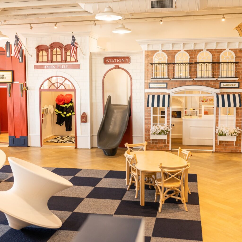Childrens play area resembling a small town with a custom designed fire station with slide, and a cafe. The clean colors and bright space make for a delightful children's indoor play cafe.