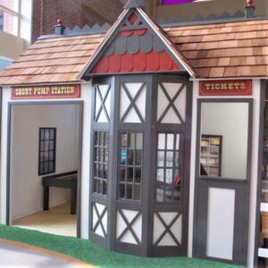 A train station playhouse with a ticket window, a bay window and a wood shingled roof is a perfect stop for children to collect their tickets before embarking on a new adventure in an indoor play town.