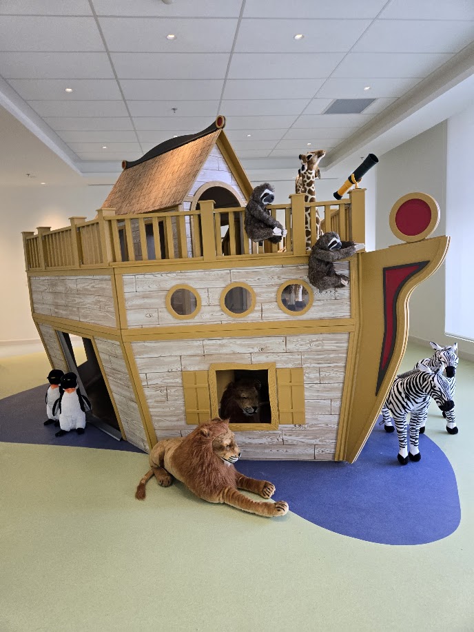A custom built child sized Arc playhouse, with faux wood, a telescope, and pairs of stuffed animals around the boat.