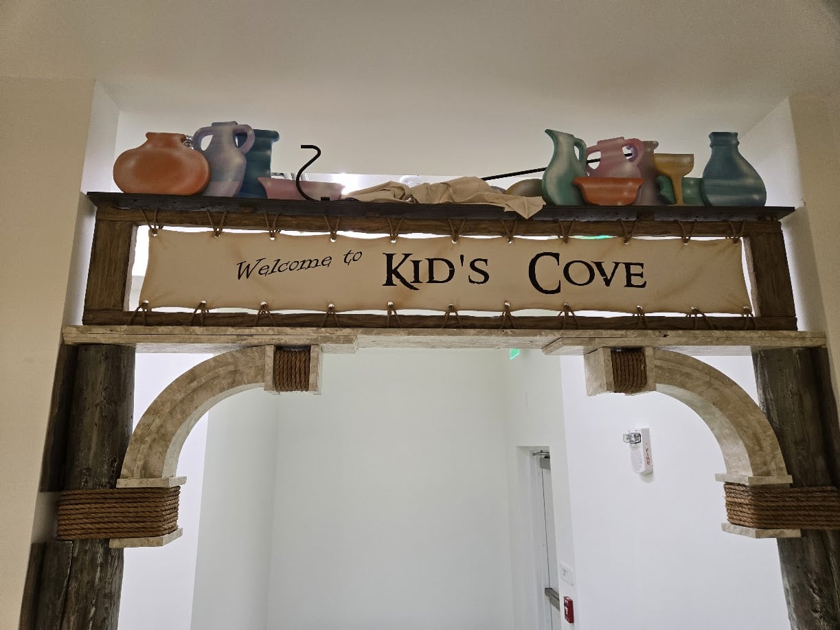A custom built sign for a church's youth area, reading "Welcome to Kid's Cove", decorated with pots and vases, and pieces of faux marble.