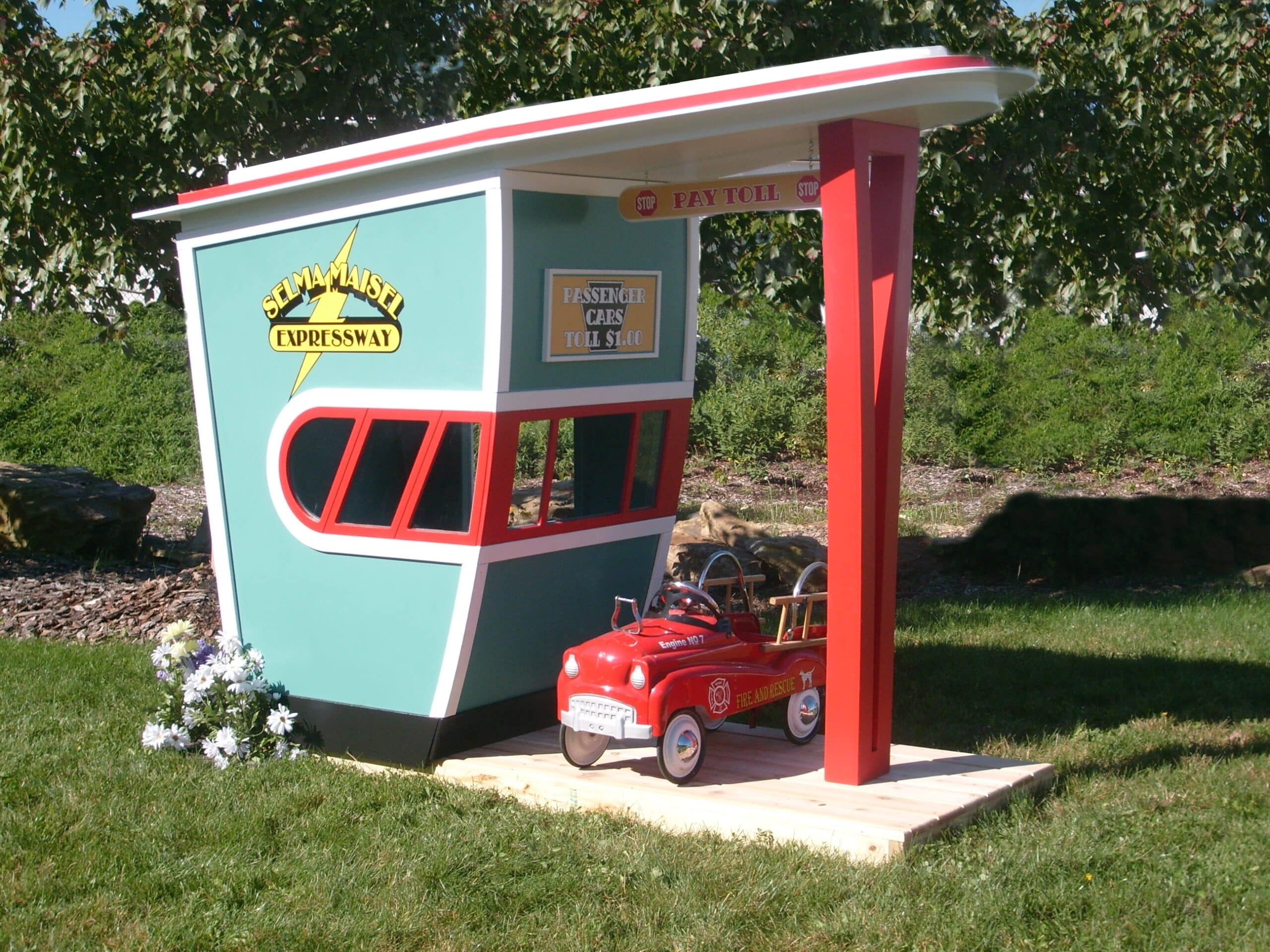 A custom child sized toll booth play house with a child sized red fire truck driving through the booth.