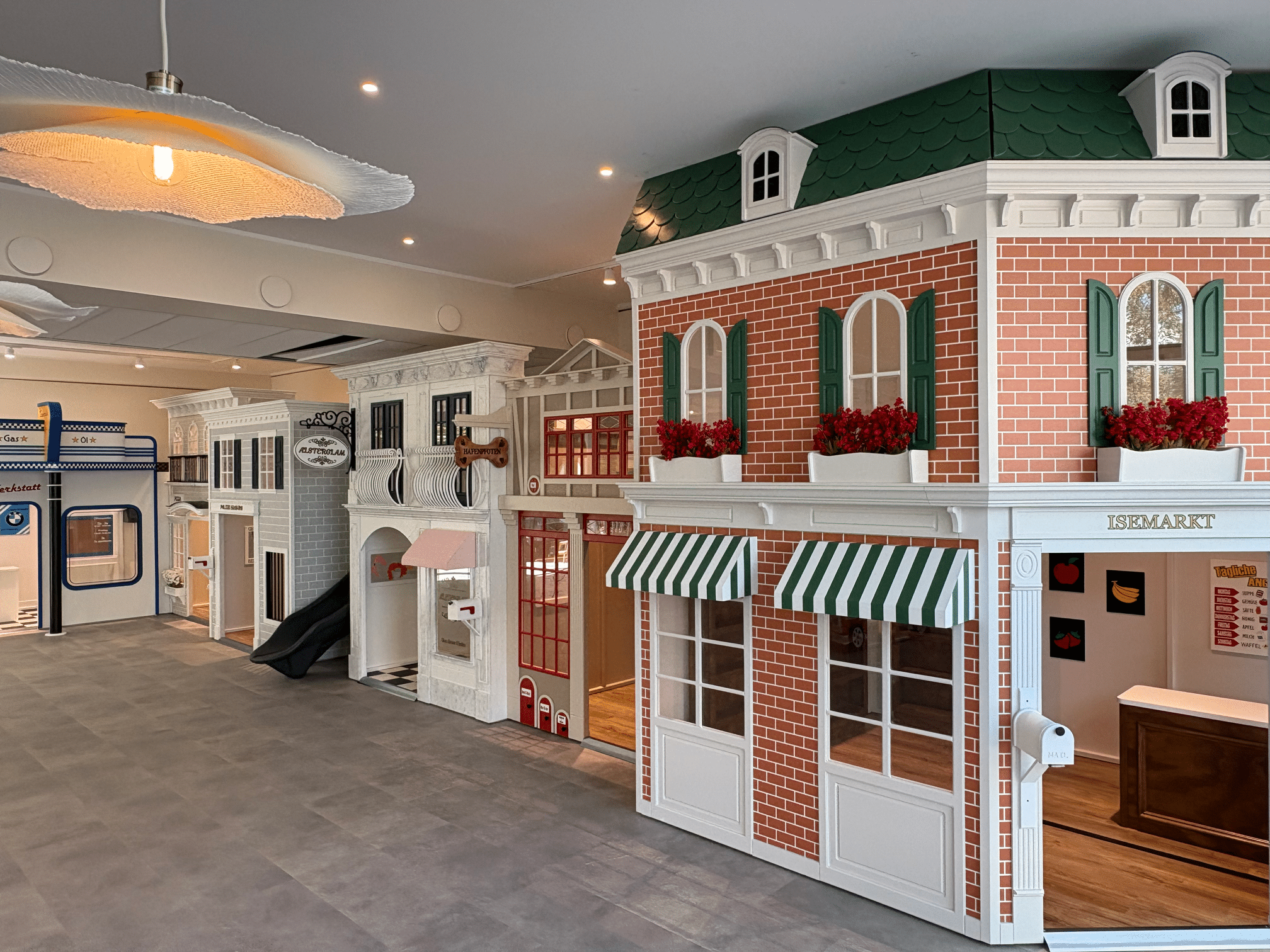Indoor play cafe in Hamburg, Germany featuring child-sized playhouses designed to resemble a town street with storefronts, a slide, and themed decor.