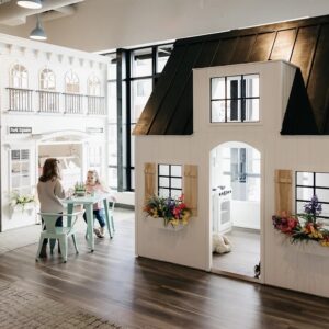 Two children sit at a small table outside of Nana's House on Main Street playhouse and other miniature buildings, such as a doctor's office and bakery.